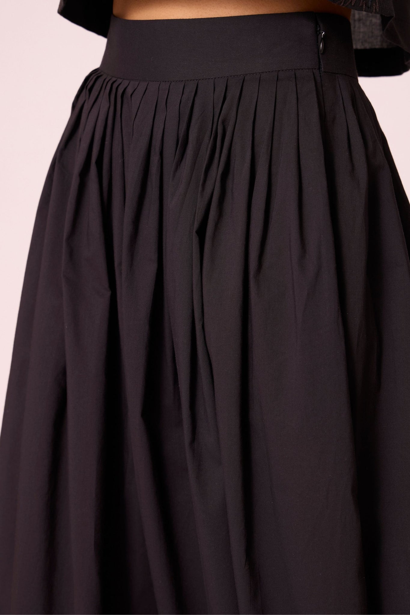 Black organic cotton pleated pants with a relaxed fit, side zip fastening, and adjustable hem cuffs.
