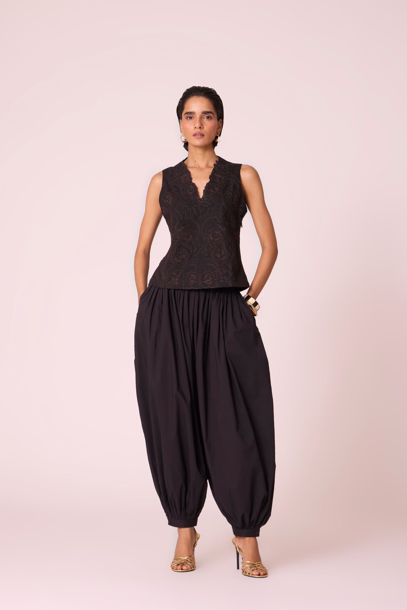 Black organic cotton pleated pants with a relaxed fit, side zip fastening, and adjustable hem cuffs.
