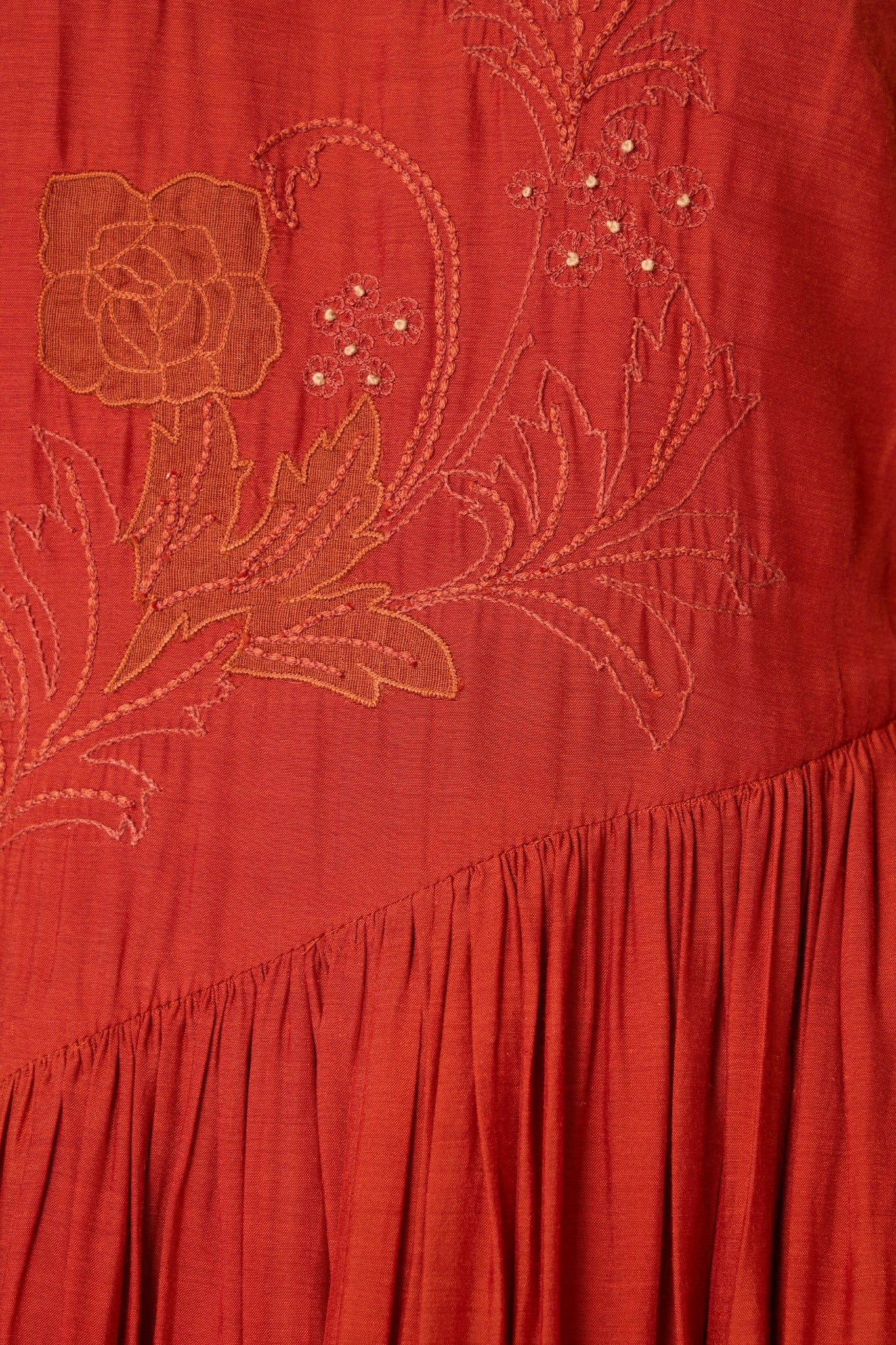 Rust cupro midi dress with hand-embroidered bodice, asymmetric gathered waist, and rouleau back button.

