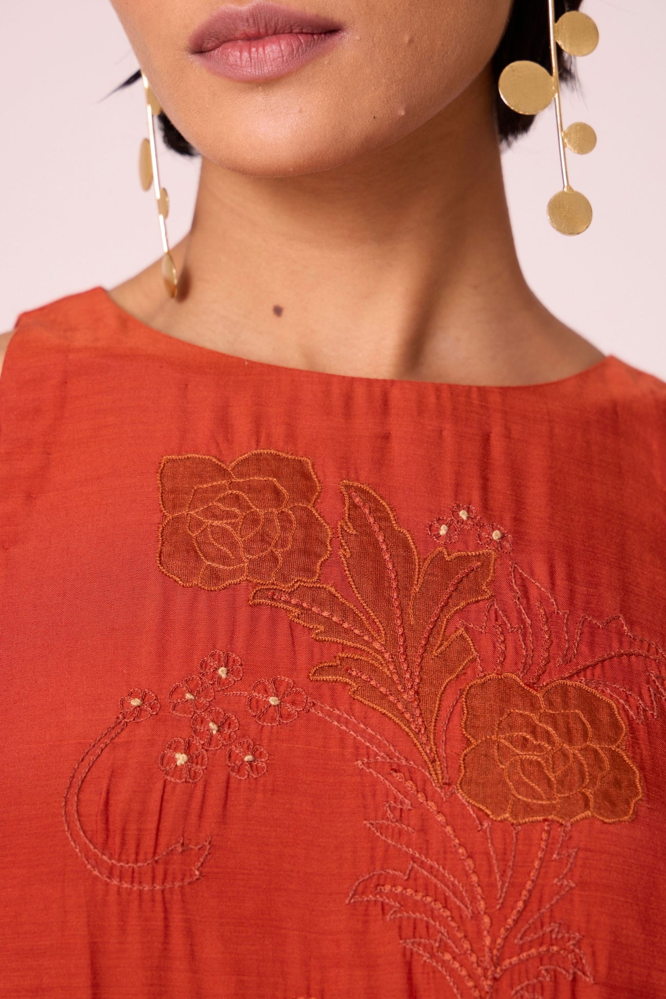 Rust cupro midi dress with hand-embroidered bodice, asymmetric gathered waist, and rouleau back button.
