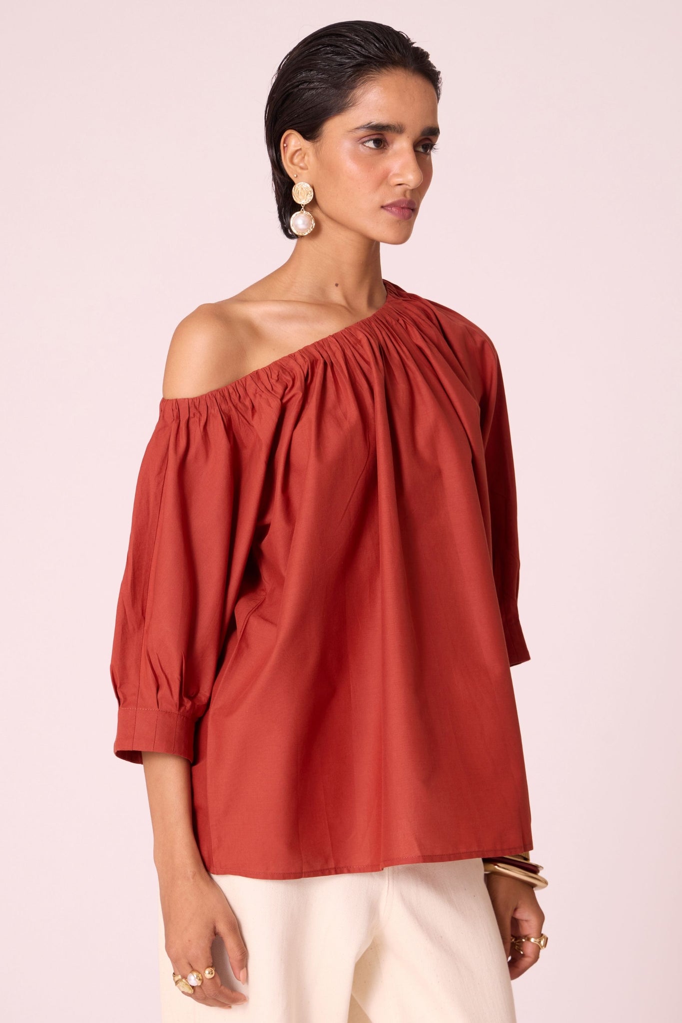 Rust organic cotton off-shoulder top with gathered neckline and pleated sleeve cuffs.