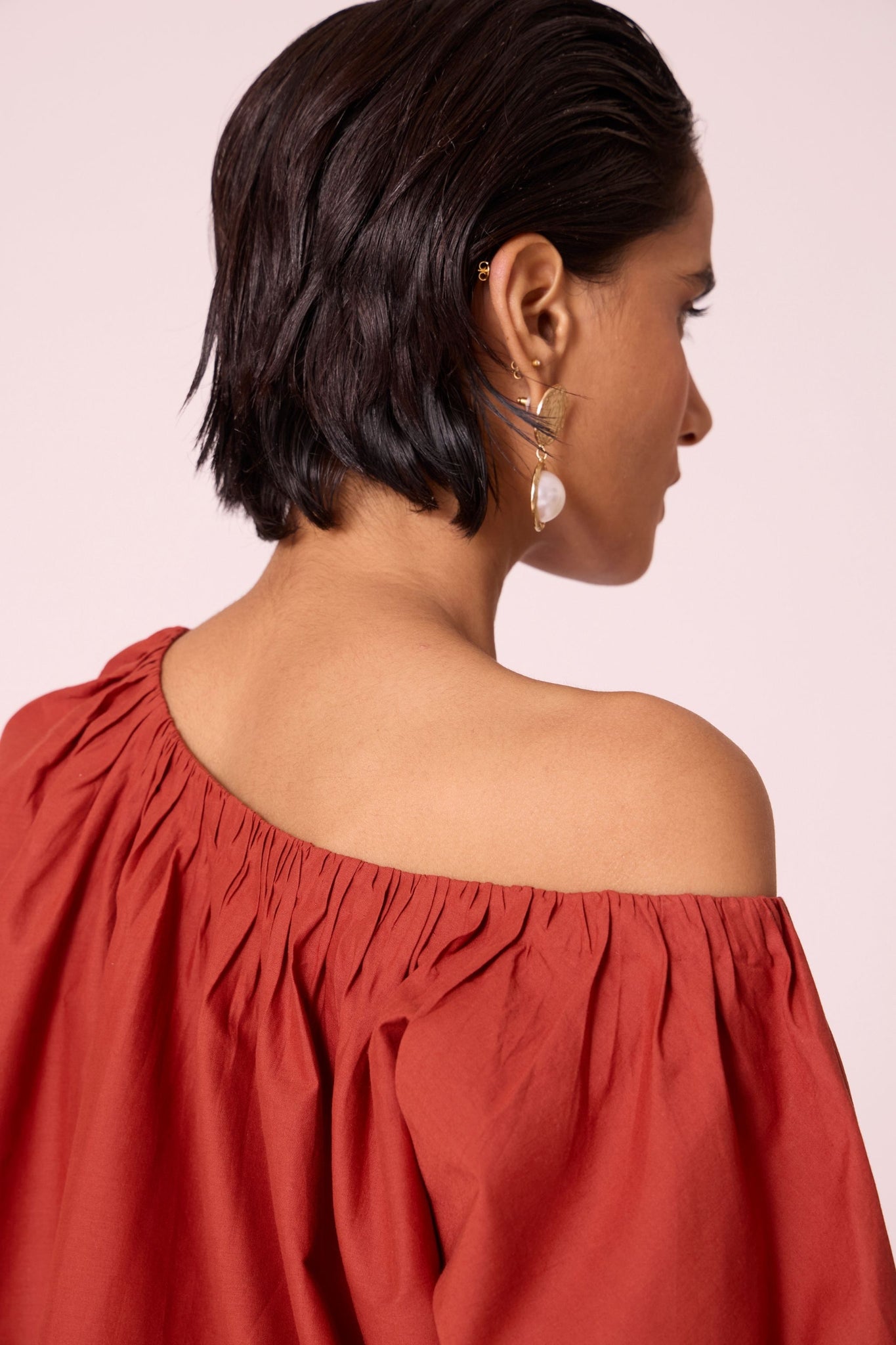 Rust organic cotton off-shoulder top with gathered neckline and pleated sleeve cuffs.