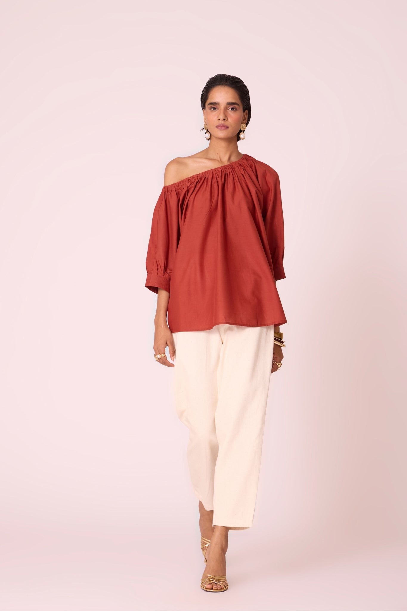 Rust organic cotton off-shoulder top with gathered neckline and pleated sleeve cuffs.