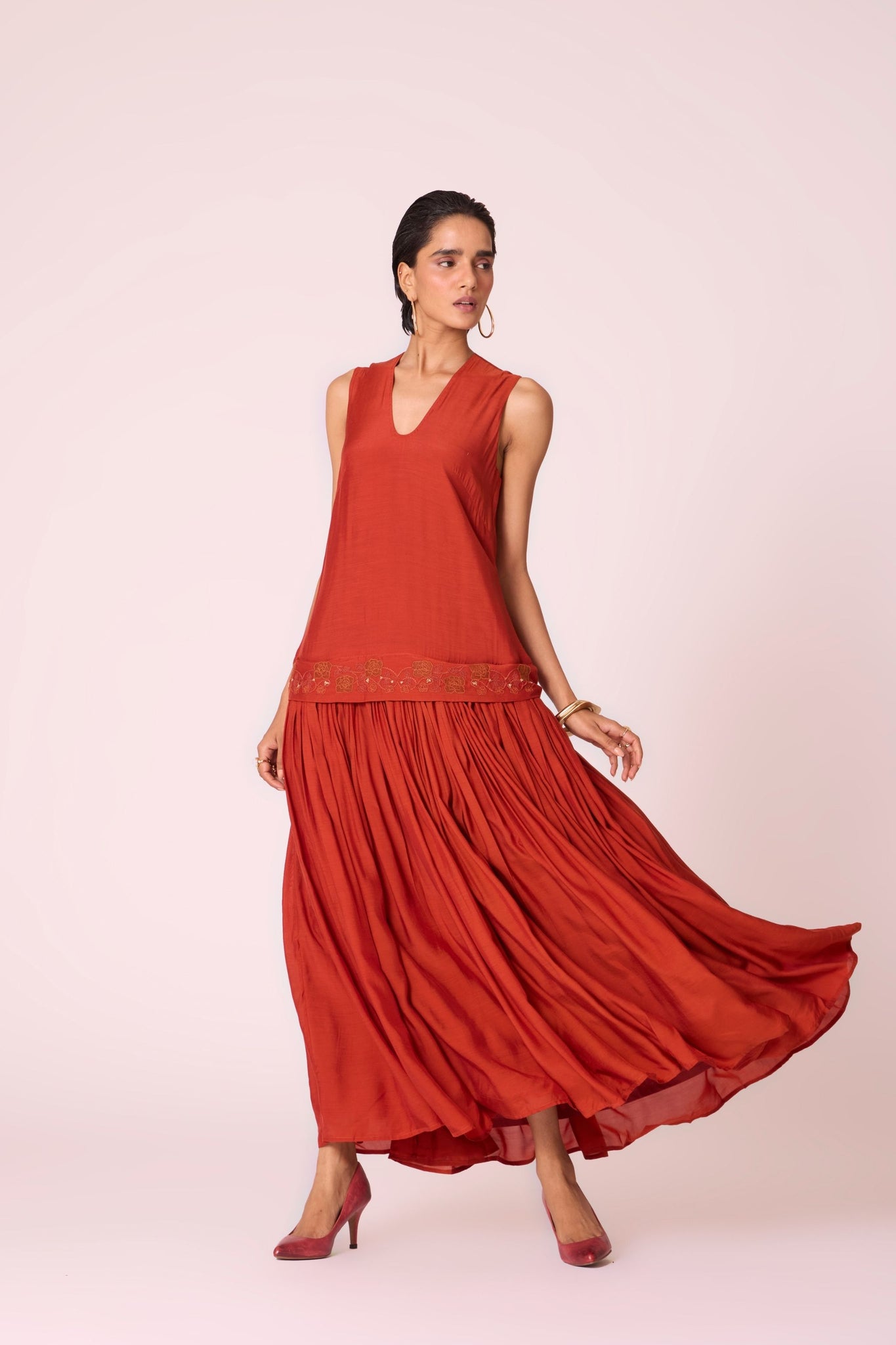 Rust cupro drop-waist dress with hand-embroidered waist, narrow scooped neckline, and full lining.

