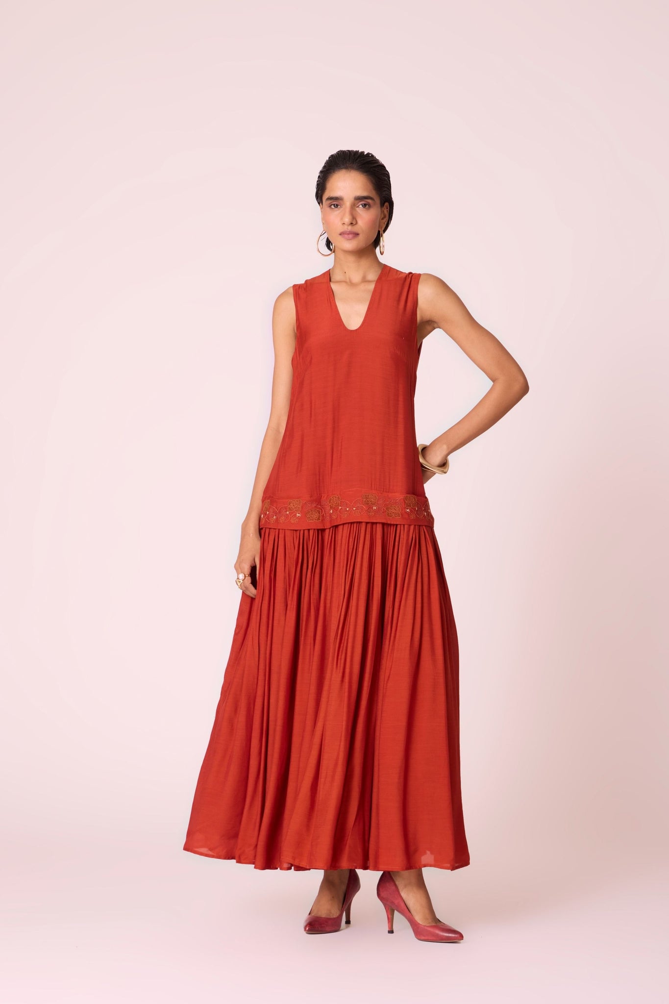 Rust cupro drop-waist dress with hand-embroidered waist, narrow scooped neckline, and full lining.
