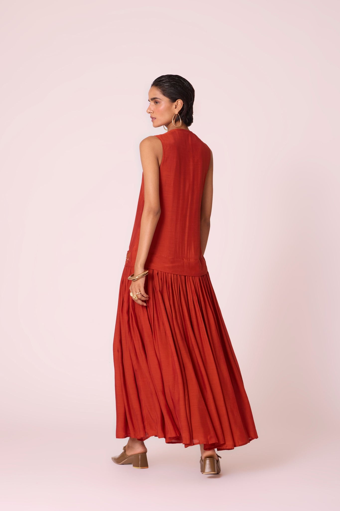 Rust cupro drop-waist dress with hand-embroidered waist, narrow scooped neckline, and full lining.
