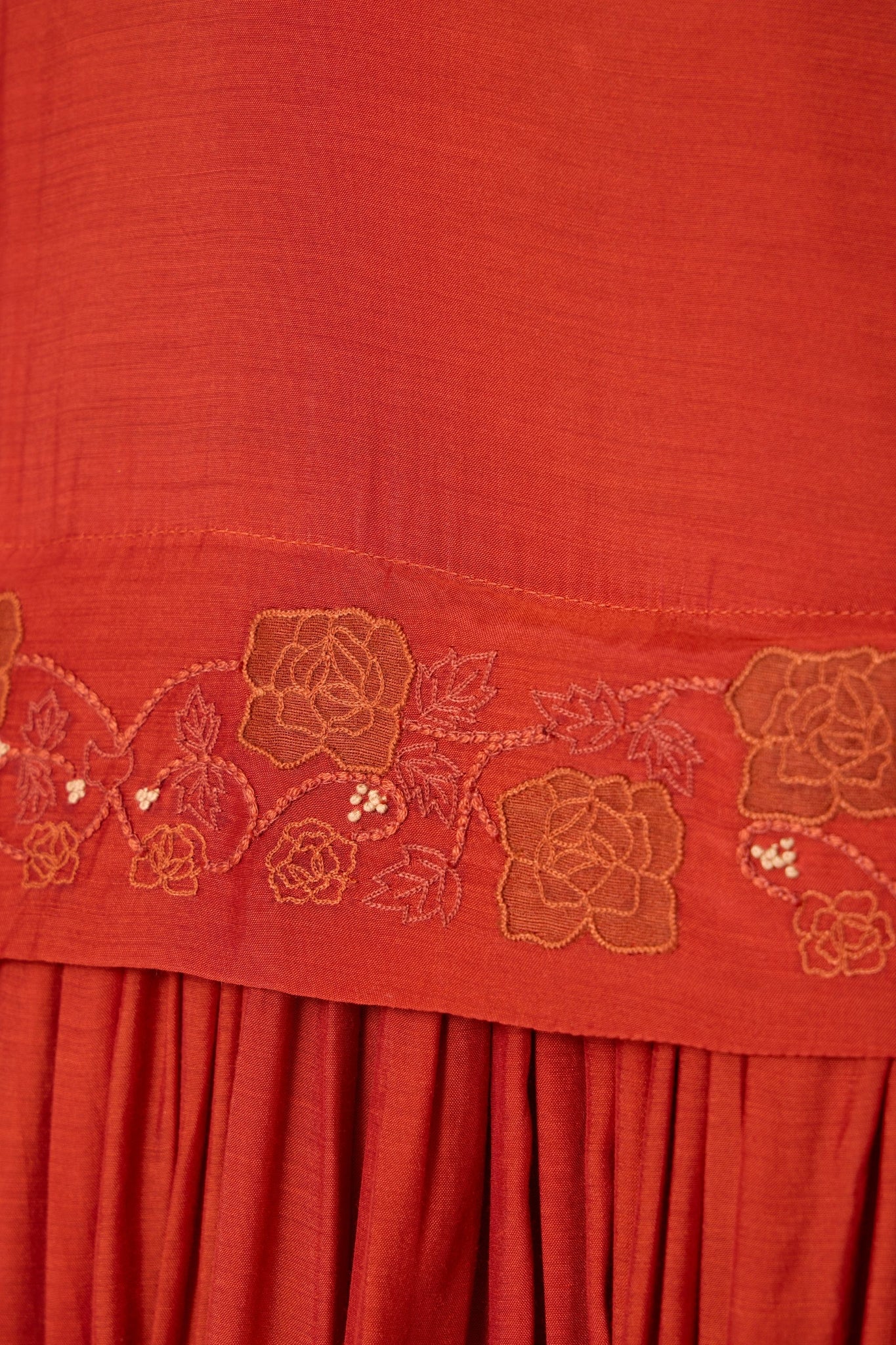 Rust cupro drop-waist dress with hand-embroidered waist, narrow scooped neckline, and full lining.
